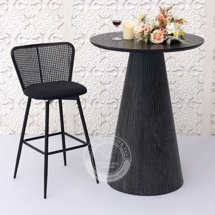 Black bar stool and round black cocktail table with decorative elements against a patterned wall.